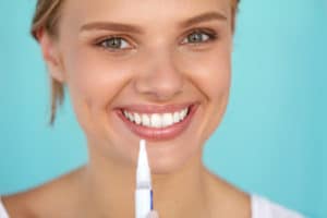 close up portrait of smiling young woman with teeth whitening gel