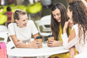 woman with porcelain veneers drinking coffee with two friends at outside table