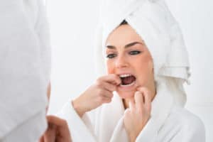 Close-up Of A Woman Looking In Mirror Flossing Teeth