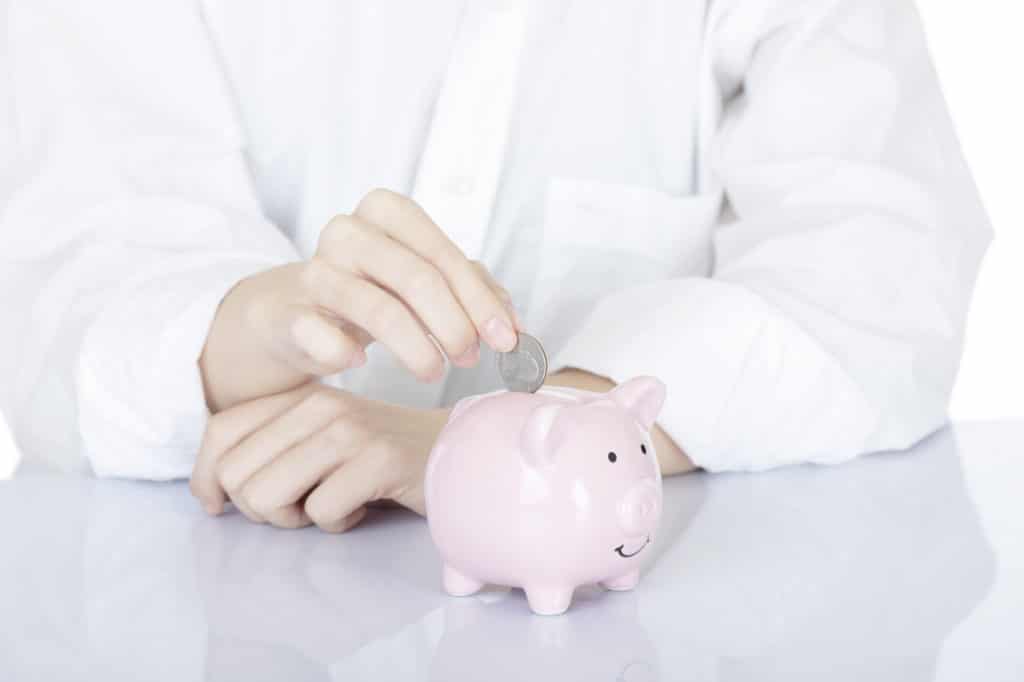 woman in white coat putting coin in piggy bank