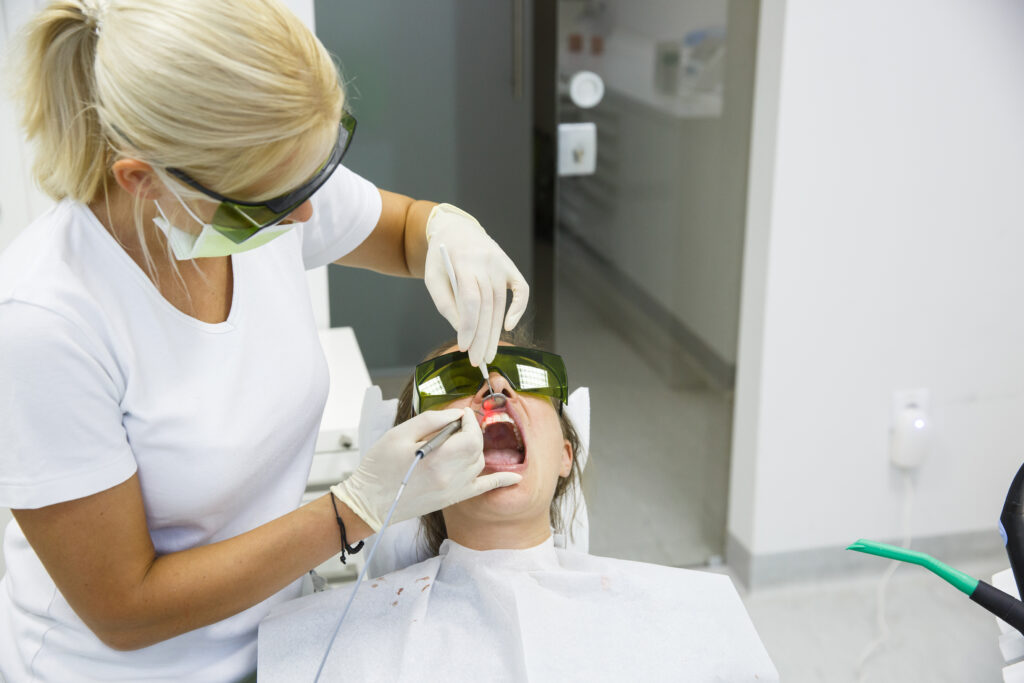 Dentist using a modern diode dental laser for periodontal care. Both wearing protective glasses, preventing eyesight damage.
