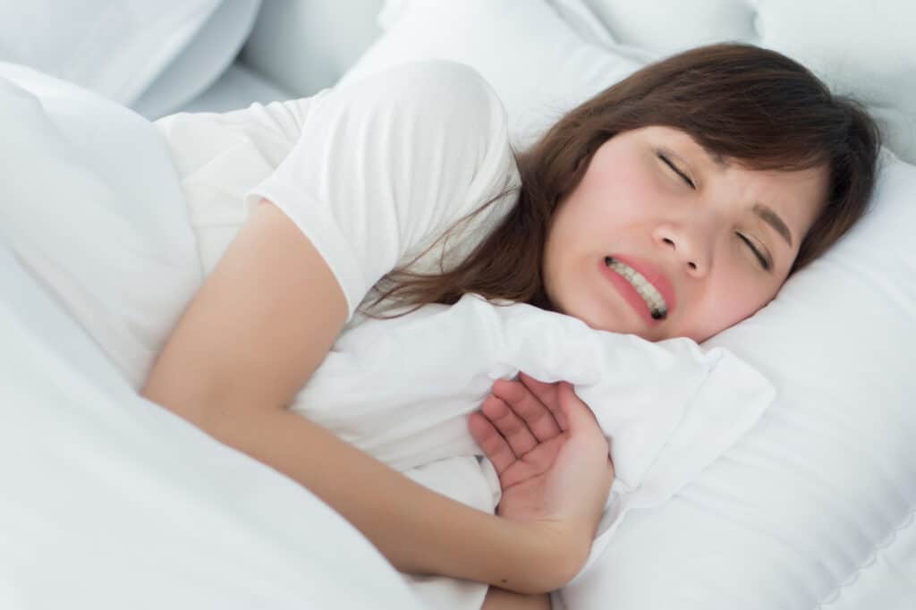 woman laying in white bed asleep and grinding her teeth