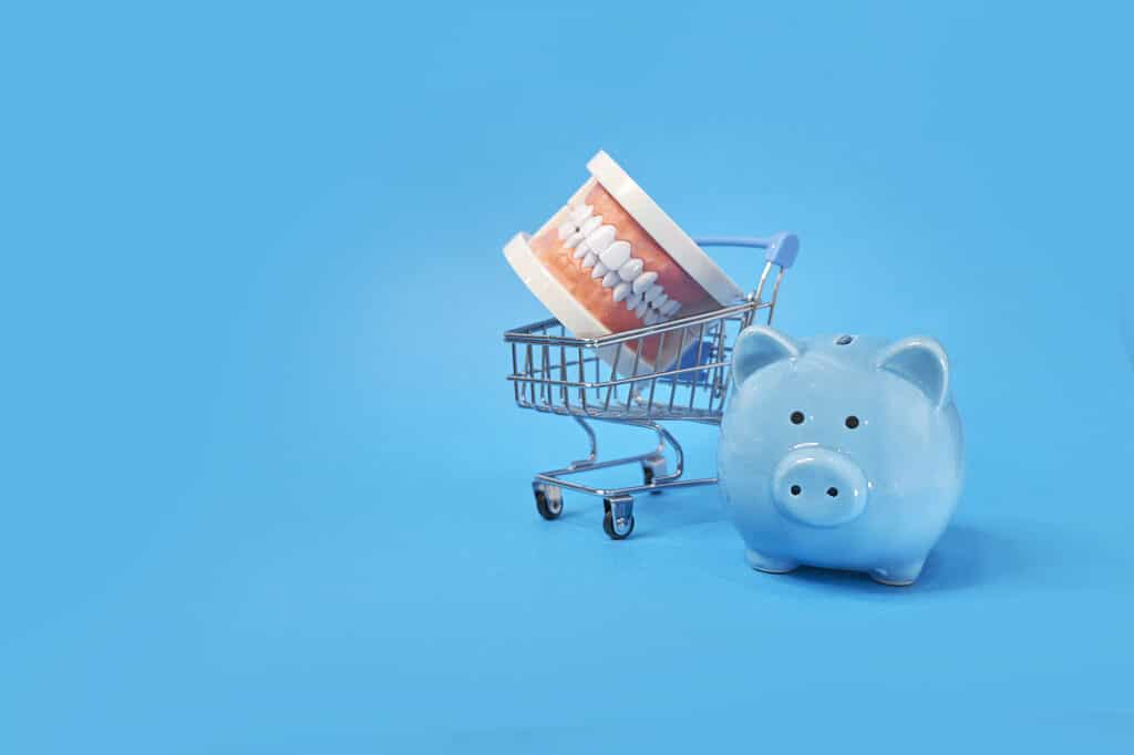 Piggy bank with White teeth model on blue background (symbolizing affordable dental care)