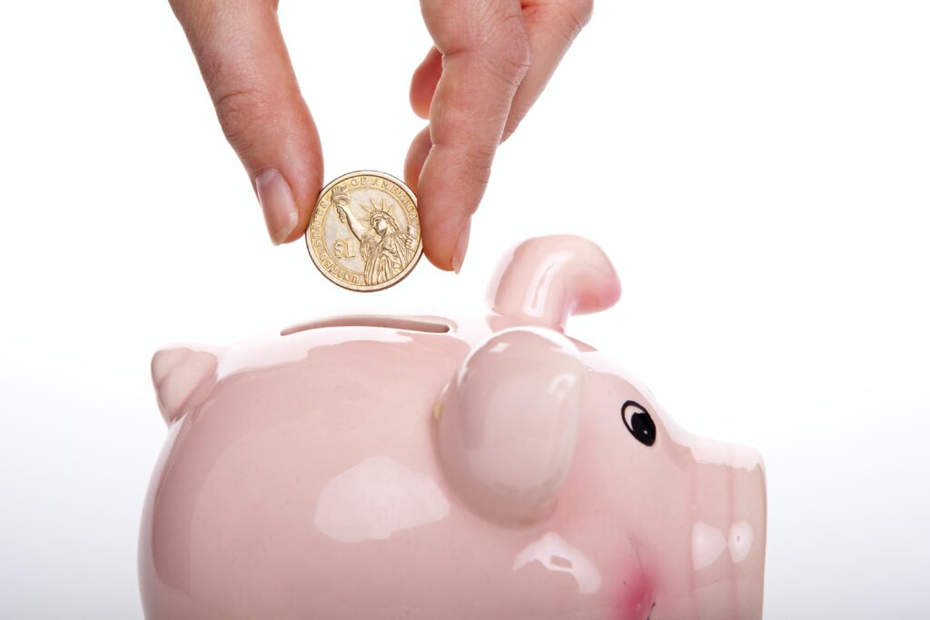 A hand places a coin into a ceramic piggy bank, indicating the monetary advantages of switching to an in-house dental plan.