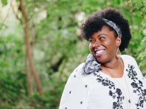 black woman smiling over her shoulder wearing a white floral shirt and headband