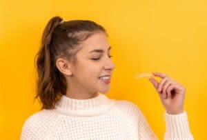 girl with yellow background looks sideways holding clear braces