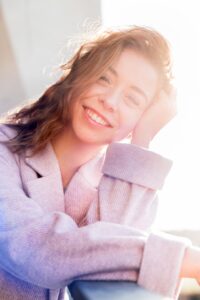 smiling girl with brown hair and gray jacket in sunlight