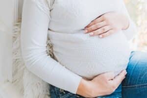 pregnant woman in white sweater holding belly