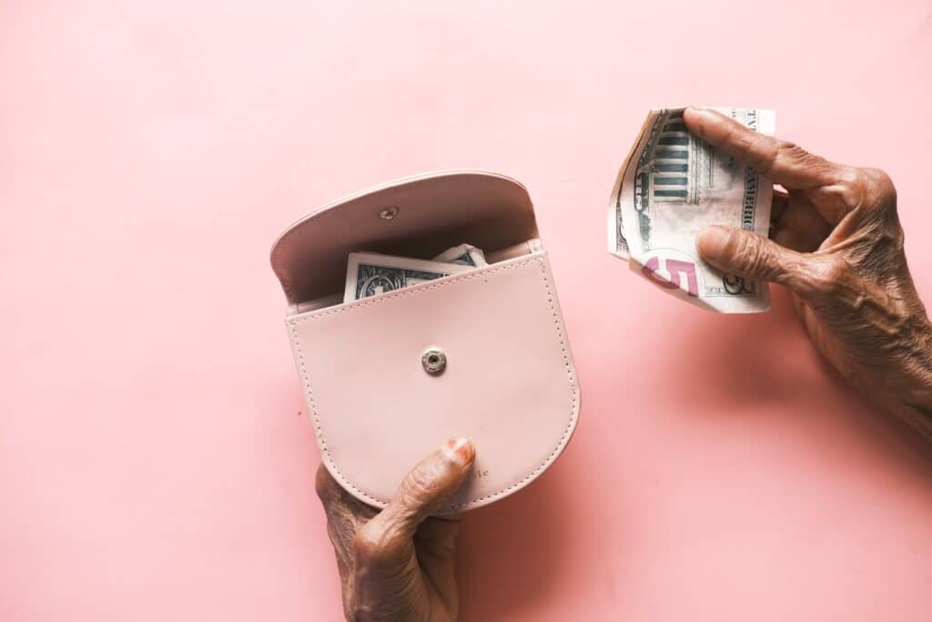 old woman's hands pulling money out of a pink wallet on pink background