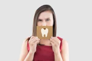 Asian woman in the red shirt holding a brown paper with the caries cartoon picture of his mouth against the gray background, Have a toothache, The concept with healthcare gums and teeth