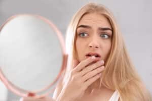woman looking in mirror covering mouth