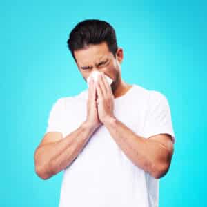 Tissue, nose and man in studio for sick allergy, cold and influenza on blue background. Asian male model sneeze wit hayfever, allergies and infection of virus bacteria, health care and congestion.