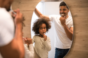 father and daughter brushing teeth in the bathroom mirror