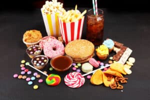 candy, donuts, French fries, popcorn, soda, hamburger on black table