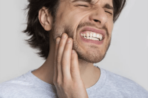 man wincing and touching his face because of tooth pain, needs restorative dentistry