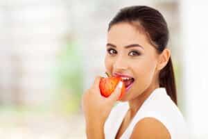 woman with dark hair looking at the camera biting into an apple