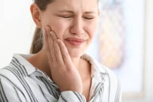 woman wincing and touching her jaw because of TMJ pain