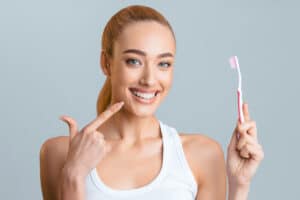 beautiful young woman pointing at her teeth and holding a toothbrush