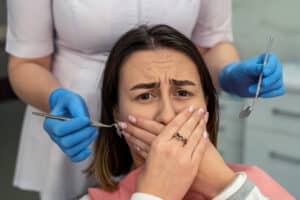 woman in dental chair with dental anxiety covering her mouth