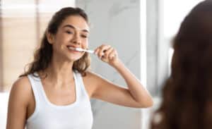 woman brushing her teeth in bathroom mirror