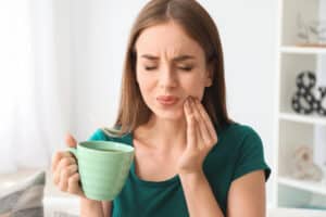 Young woman with sensitive teeth and cup of hot coffee at home