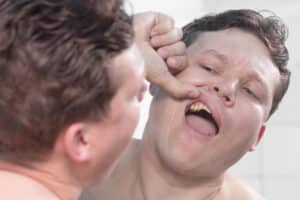 man looking at his teeth in the mirror