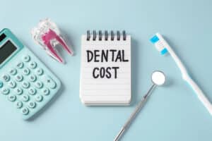 notepad with "dental cost", calculator, and dental tools on a table